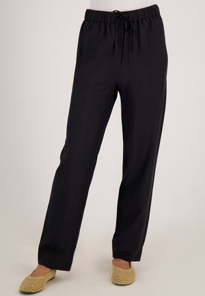 Zwarte, loszittende broek met een elastische tailleband en trekkoord. Lichtgewicht stof met verticale textuur. Gepaard met beige gevlochten flats.