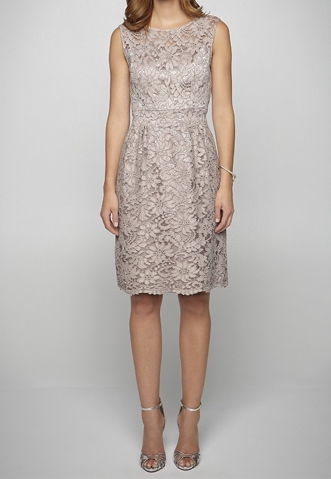Robe beige en dentelle sans manches, longueur genou, avec motif floral, portée avec des sandales argentées à talons hauts et un bracelet au poignet droit.