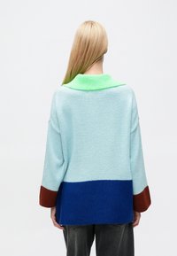 Light blue knitted sweater with a green collar, featuring color-block sections in dark blue and brown on the sleeves and bottom.