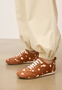 Pruunide täppidega tossud tekstuuriga karvasest nahast, valgete paelte ja kummitaldadega, sobituvad beežide pükstega.