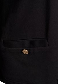 Svart tygplagg med en sidficka och en guld, texturerad knapp. Slät yta, strukturerad form med minimalistiska design detaljer.