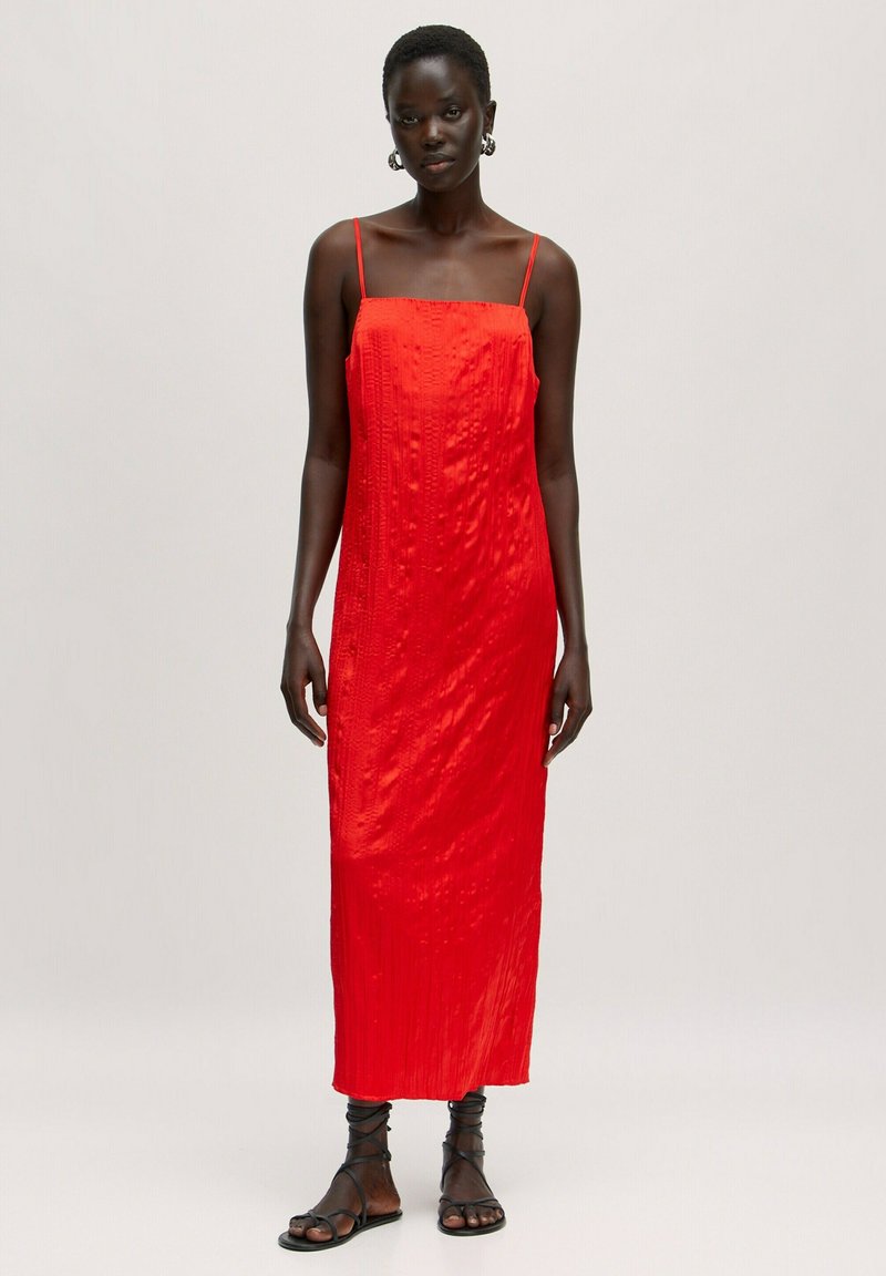 Rotes, ärmelloses Maxikleid mit strukturiertem Oberflächen, geradem Schnitt und dünnen Trägern. Getragen mit schwarzen Riemchensandalen.