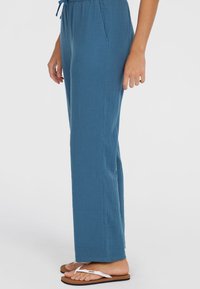 Light blue, wide-leg pants with an elastic waistband, textured fabric, two side pockets, and paired with flip-flops.