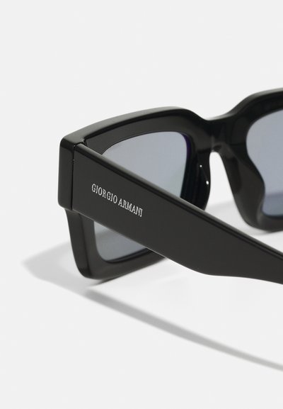 Black sunglasses with angular frames, featuring mirrored lenses and brand logo "Giorgio Armani" embossed on the side. Smooth texture and solid design.