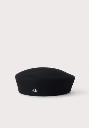 Béret en laine noire avec de petites initiales "RB" blanches brodées à l’avant sur un fond clair uni.