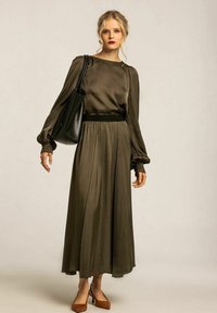 Olivgrön satin långärmad klänning med snäv midja och flödande kjol. Svart handväska och bruna blockklackskor fulländar looken.