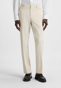 Beige skräddarsydda byxor med slät textur, rak benstil och platt framdesign. Bärs med svarta loafers och en vit skjorta.