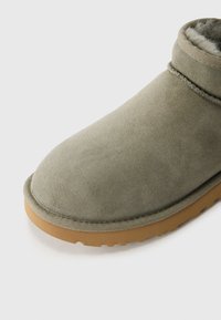 Primer plano de una bota de ante marrón claro con una suela de goma color chicle y un forro de suave lana de felpa visible dentro del collar del tobillo.