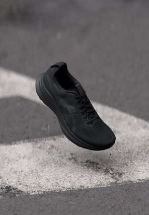 Schwarzer Sportschuh in der Luft über Asphaltfläche mit weiß gemalten Straßenmarkierungen und kleinen verstreuten Trümmern.