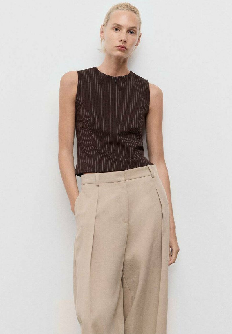 Top senza maniche a righe marroni abbinato a pantaloni beige a vita alta plissettati, caratterizzati da un tessuto liscio e linee pulite.