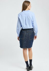 Chemise rayée bleu clair avec un pli au dos, associée à une jupe crayon en denim foncé avec deux poches arrière et des coutures contrastantes.