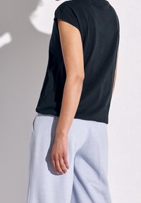 Svart kortärmad t-shirt sedd från baksidan, ihop med ljusgråa sweatpants. T-shirten har en avslappnad passform och mjuk textur.