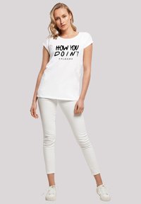 White cotton t-shirt featuring the text "HOW YOU DOIN'?" in bold black, paired with white fitted pants and white sneakers.