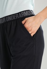 Svarta träningbyxor med bred elastisk midja som har "UNDER ARMOUR" i grått. Sidofickor och mjukt, stretchigt tyg.