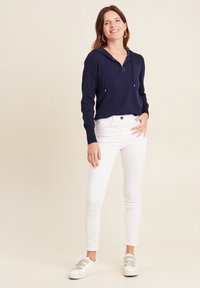 Marineblauer Hoodie mit Reißverschluss am Hals, kombiniert mit weißen Slim-Fit-Jeans und weißen Sneakers. Der Stoff wirkt weich; das Design ist lässig und bequem.