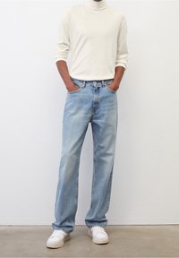 Hellbeige Rollkragenpullover, lockere Passform. Blaue weit geschnittene Jeans mit einem ausgewaschenen Look, Fünf-Taschen-Design und dezenten Nähten. Weiße Sneakers.