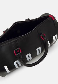 Fekete bőrből készült utazótáska fehér felirattal, piros cipzárdíszítéssel és rövid fogantyúkkal. Tágas, sötét belső térrel rendelkezik.