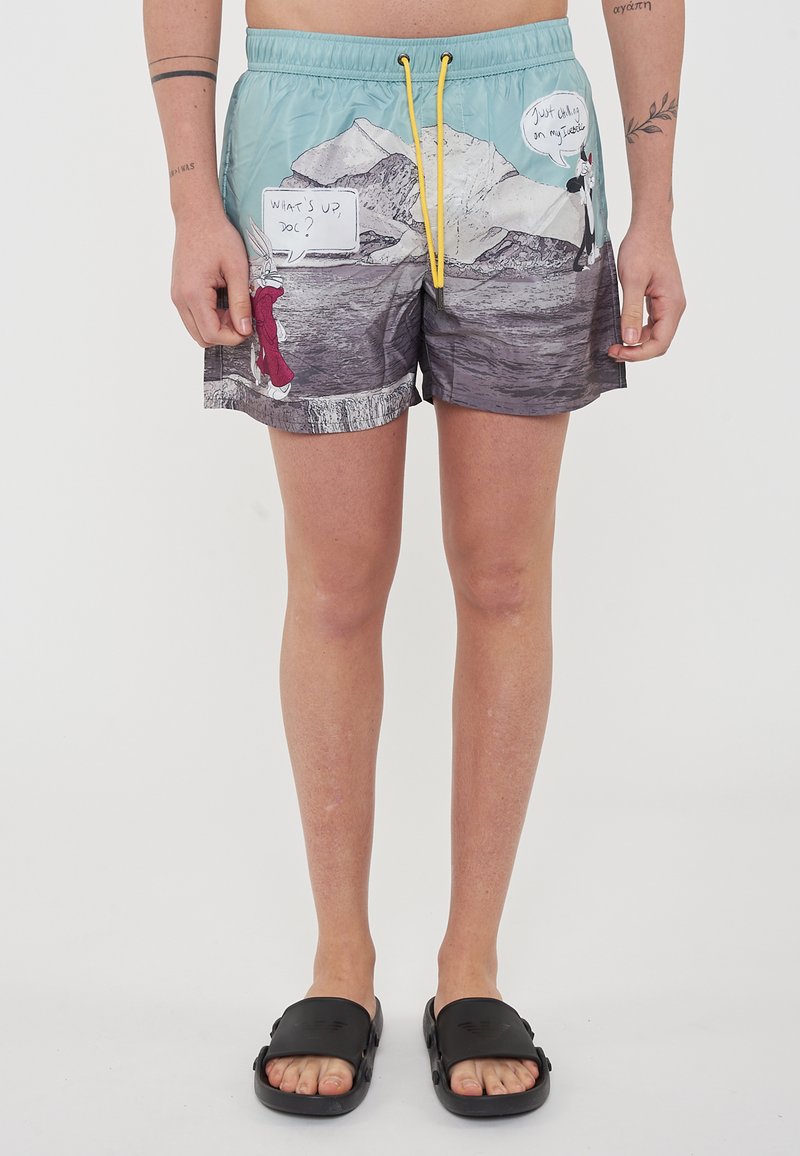 Costume da bagno in azzurro chiaro con grafiche di cartoni animati. Presenta un design in bianco e nero all'orlo. Vita elastica con cordino giallo.