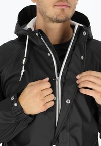 Czarna wodoodporna kurtka z kapturem ze ściągaczem, zamkiem błyskawicznym z przodu i zatrzaskami. Posiada elastyczne mankiety oraz kontrastową białą podszewkę.