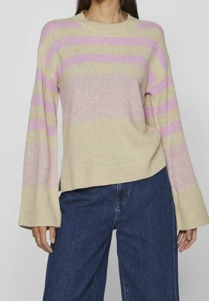 Beige gebreide trui met roze strepen, ronde hals en uitlopende mouwen. Zachte textuur met een losse pasvorm, gecombineerd met donkerblauwe flared jeans.