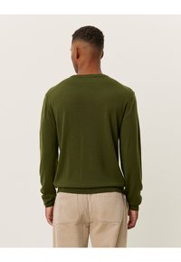 Pulover tricotat verde cu guler rotund și manșete cu nervuri, prezentând o textură netedă. Afișat din spate, asortat cu pantaloni din catifea ușor colorați.
