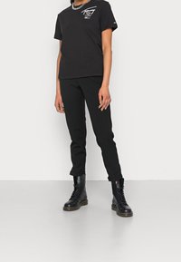 Svart bomullströja med vit grafisk print, kombinerad med svarta tapered byxor och svarta snörda kängor. Enkel design, inga mönster.