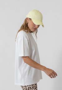 Valge puuvillane T-särk lõdva istuvusega, kombineeritud heledat kollasest pesapalli mütsist ja loomade mustriga pükstest. Minimalistlik disain, igapäevane stiil.