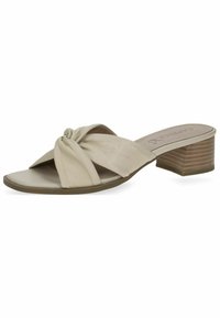 Beige heeled sandals featuring a knotted strap design, a smooth leather texture, and a low stacked heel for support and comfort.