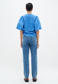 Ljusblå blus med puffärmar kombinerad med högmidjade, rakbenade blå jeans. Jeansen har en klassisk femficksdesign och en subtil fade.