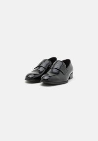 Pantofi din piele neagră cu o finisare lucioasă, având o curea lată pe partea superioară și un vârf rotund. Toc mic pentru stabilitate.