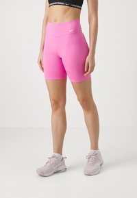 Shorts de sport roses en tissu extensible avec une taille haute, associés à des baskets Nike rose clair. Design simple sans motifs.