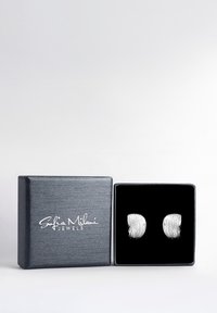 Silvriga strukturerade studörhängen visade i en svart sammetsfack, förpackade i en matt mörkblå låda med vit märkning.