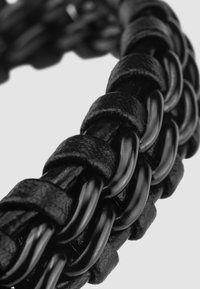 Black woven bracelet featuring interlacing leather and glossy metal links, showcasing a textured finish and smooth contours.
