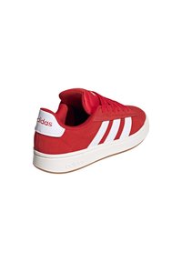 Rote Wildleder-Sneaker mit weißer Gummisohle, die drei weiße Streifen an der Seite und weiße Markenkennzeichnung an der Ferse und der Zunge aufweist.