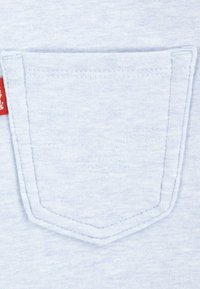 Tejido azul claro con un bolsillo cosido de cima puntiaguda y una etiqueta de color rojo. Textura suave con un sutil patrón jaspeado.