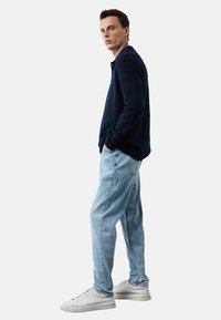 Granatowy sweter dzianinowy, jasnoniebieskie luźne dżinsy i białe trampki. Sweter ma kołnierzyk i ryflowane mankiety, a dżinsy charakteryzują się luźnym krojem.