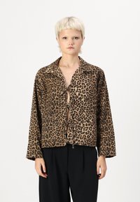 Jasje met luipaardprint van zachte stof, met een kraag, sluiting met strik aan de voorkant en twee voorzakken. Korte, losjes zittende mouwen.