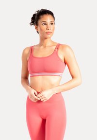 Różowy sportowy stanik na cienkich ramiączkach, z szerokim pasem ozdobionym paskowanym akcentem. Materiał wydaje się gładki i rozciągliwy.