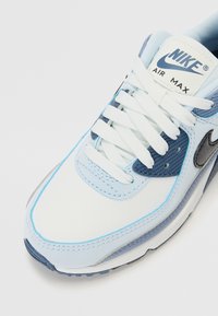 Adidașii Nike Air Max au un design cu un superior din piele albă și plasă de culoare bleu deschis, accente gri și șireturi albe. Logo-ul brandului se află pe limbă.