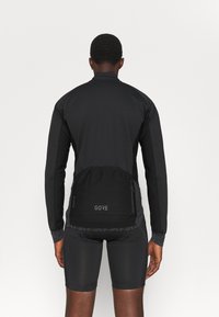 Czarna kurtka rowerowa z wysokim kołnierzem, ergonomicznym krojem i tylną kieszenią. Wykonana z lekkiego, elastycznego materiału z odblaskowymi akcentami.