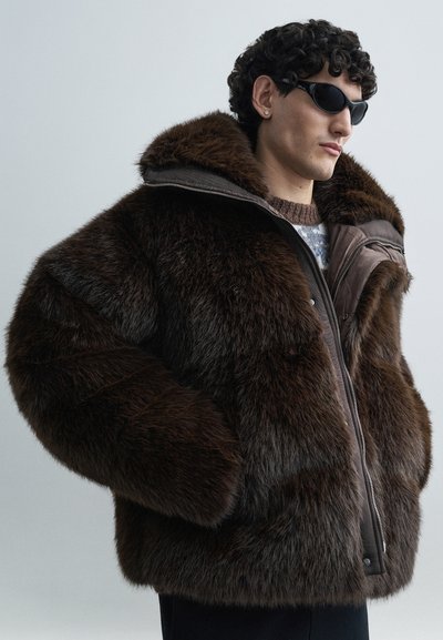 Brown faux fur puffy jacket with a detachable hood, large pockets, and a zipper closure. Features textured surface and a relaxed fit.