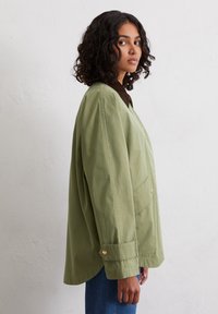 Green oversized jacket with a brown collared neckline, featuring gold buttons, side pockets, and a smooth, textured fabric.