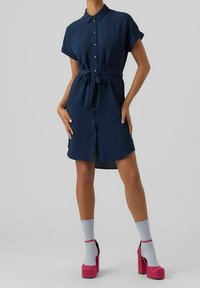 Abito camicia blu navy a maniche corte con apertura a bottoni e vita regolabile con corda. Abbinato a lunghe calze bianche e tacchi a piattaforma rosa. Tessuto morbido.