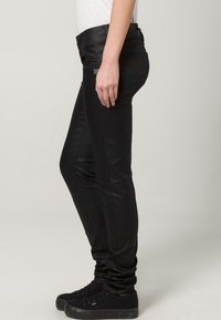 Svarta slim fit jeans med en slät, stretchig textur, som har en klassisk femfickdesign och en medelhög midja. I kombination med svarta sneakers.