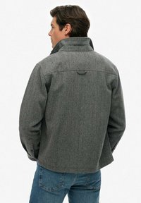 Grau kariertes Jackett mit hohem Kragen, geknöpften Manschetten und strukturiertem Finish, getragen über klassischen blauen Jeans.
