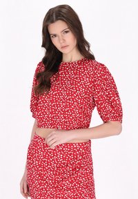Piros crop top puff ujjal, fehér virágmintával, sima textúrával. Egy hozzá illő szoknyával párosítva, így egy harmonikus szettet alkot.