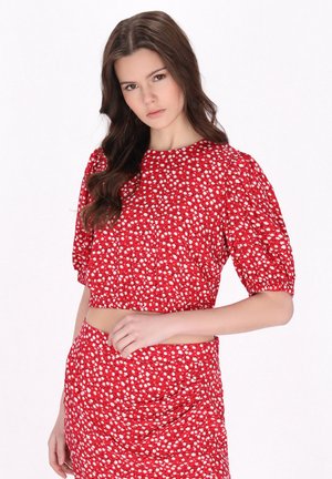 Rød cropped top med puffærmer, hvidt blomster mønster, glat tekstur. Kombineret med en matchende nederdel, hvilket skaber et koordineret outfit.