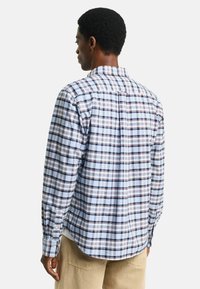 Long-sleeve checkered shirt in light blue, featuring navy and burgundy plaid pattern, button cuffs, and a curved hem. Cotton material.