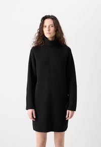 Čierne rebrované pletené šaty s vysokým rolákom, dlhým rukávom a uvoľneným strihom, siahajúcim do polovice stehna. Minimalistický dizajn bez vzorov.