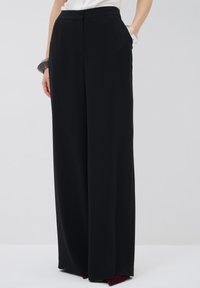 Zwarte wijde broek van zachte stof, met een hoge tailleband en zijzakken, ontworpen voor een relaxte pasvorm.